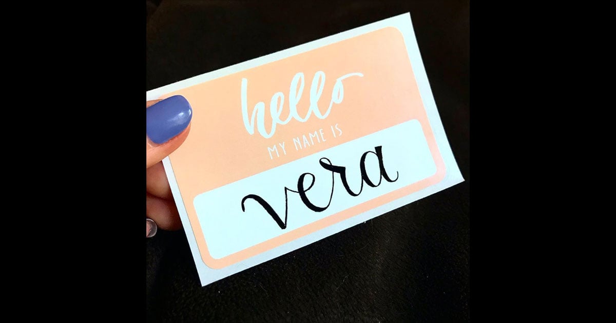 Name tag example, pulled from @moonlitdesignco: simple, "hello my name is" name tag sticker in pastel pink/salmon with calligraphic name